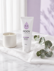 MOOV Moisture Body Cream 50g วางบนผ้าลินินขาวบนหินอ่อน ข้างเทียนอุ่นละมุนและใบยูคาลิปตัสสดชื่น สะท้อนประสบการณ์ Warm-to-Cool Sensation จาก MOOV Luxury Life-Tech Skincare